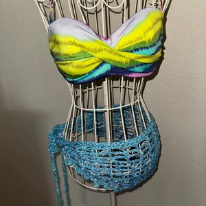 May include: A colorful bikini top and matching waist wrap displayed on a white wire mannequin. The top features a vibrant abstract design with yellow, blue, and purple hues. The waist wrap is a light blue, open-weave design.