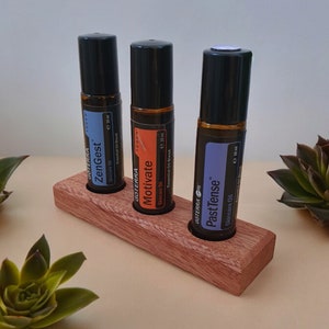 May include: Three brown glass essential oil roller bottles with black caps are displayed in a wooden holder. The bottles are labelled "ZenGest", "Motivate", and "Past Tense".