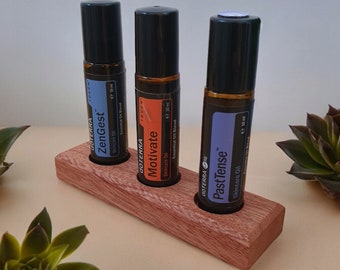 May include: Three brown glass essential oil roller bottles with black caps are displayed in a wooden holder. The bottles are labeled "ZenGest", "Motivate", and "Past Tense".