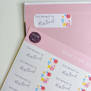 May include: A sheet of colourful, personalised name labels with the text "This belongs to Miss Rhead" and a whimsical design featuring stars, hearts, and swirls.