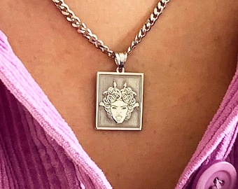 May include: A silver chain necklace with a square pendant featuring a detailed image of a woman's face with a crown of leaves.