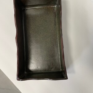 May include: A rectangular ceramic dish with a dark green glaze and a brown rim. The dish has an irregular, wavy edge.