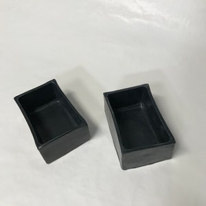 May include: Two black rectangular ceramic planters with slightly curved edges. The planters are empty and have a smooth, matte finish.