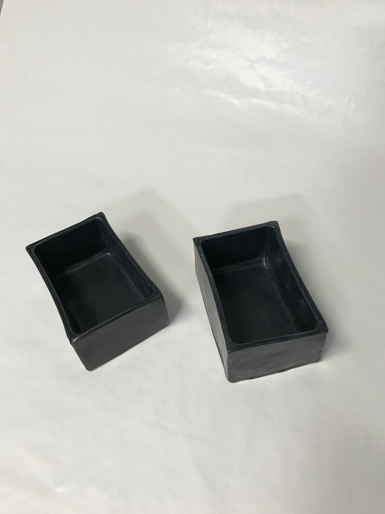 May include: Two black rectangular ceramic planters with slightly curved edges. The planters are empty and have a smooth, matte finish.
