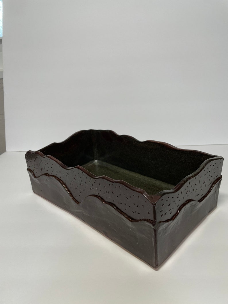 May include: A dark brown ceramic rectangular planter with a wavy rim and a speckled glaze.