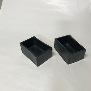 May include: Two black rectangular ceramic planters. The planters are made of a smooth, matte material and have a slightly rounded edge.