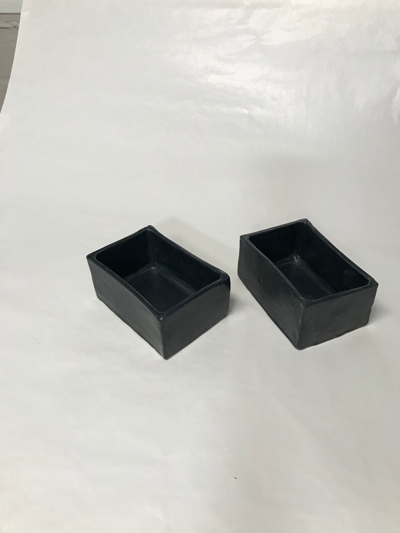 May include: Two black rectangular ceramic planters. The planters are made of a smooth, matte material and have a slightly rounded edge.