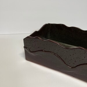 May include: A dark brown rectangular ceramic dish with a wavy, textured rim. The dish has a dark green interior.