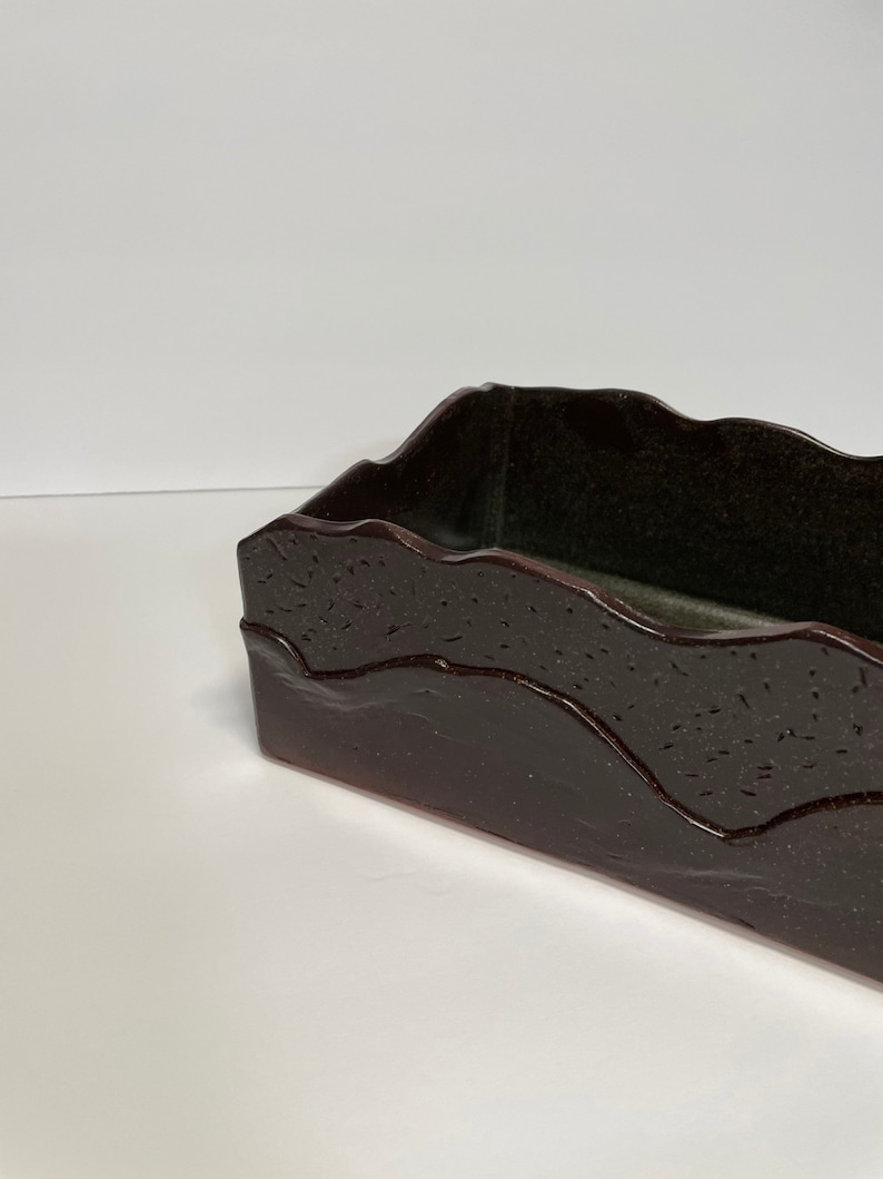May include: A dark brown rectangular ceramic dish with a wavy, textured rim. The dish has a dark green interior.