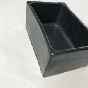May include: A black rectangular ceramic planter with a slightly rounded edge. The planter is empty and has a matte finish.