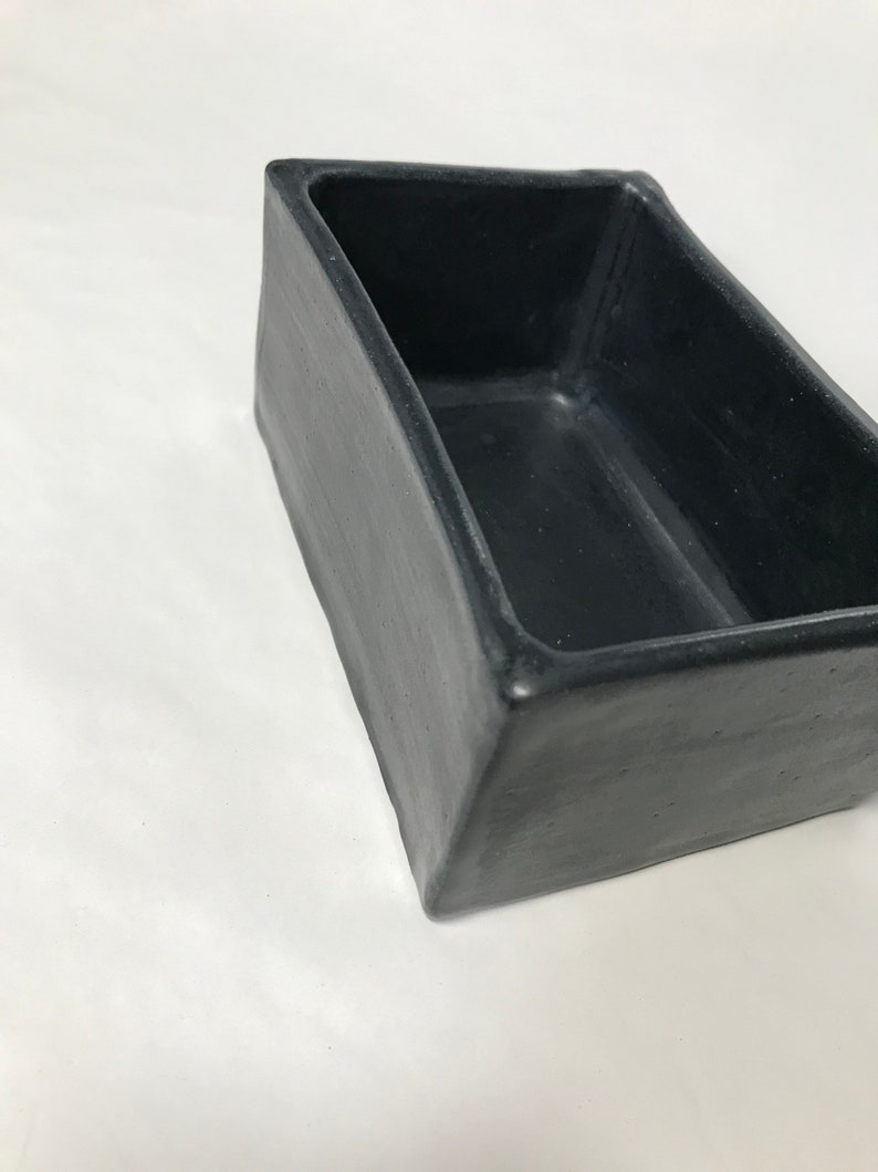 May include: A black rectangular ceramic planter with a slightly rounded edge. The planter is empty and has a matte finish.
