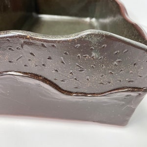 May include: A dark brown ceramic planter with a wavy rim and a speckled glaze. The planter has a rectangular shape and is made of stoneware.