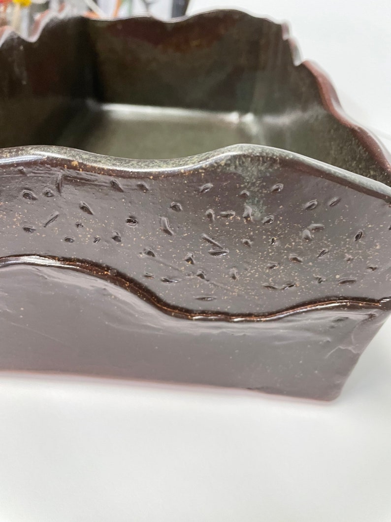 May include: A dark brown ceramic planter with a wavy rim and a speckled glaze. The planter has a rectangular shape and is made of stoneware.