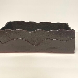 May include: A dark brown rectangular ceramic planter with a wavy, textured rim. The planter has a subtle iridescent sheen.