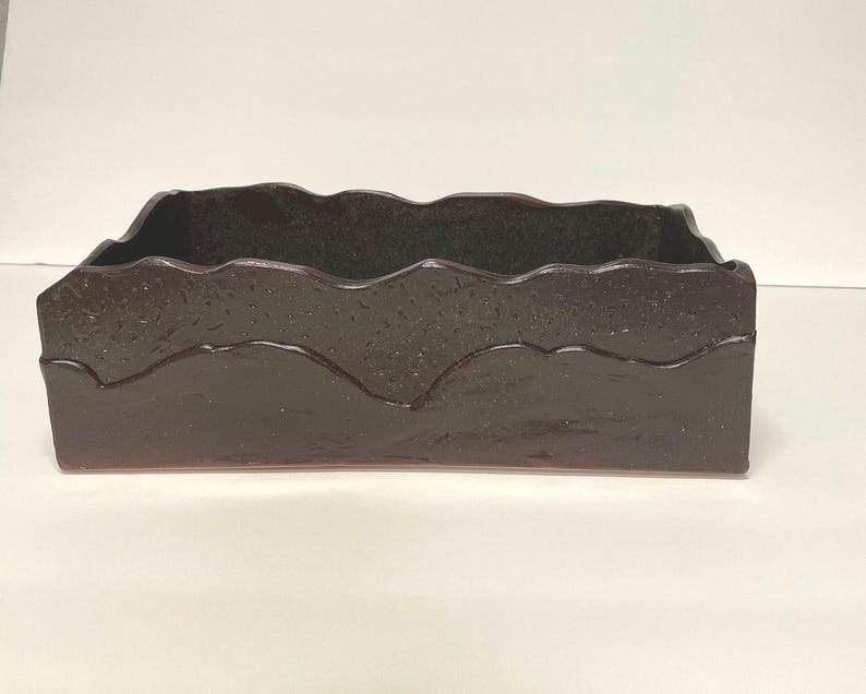 May include: A dark brown rectangular ceramic planter with a wavy, textured rim. The planter has a subtle iridescent sheen.