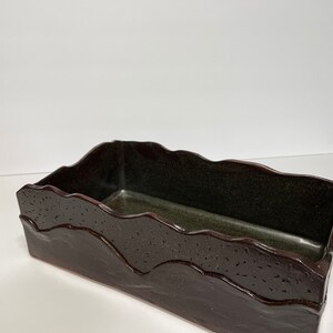 May include: A rectangular ceramic planter with a dark brown glaze and a wavy, textured rim. The planter has a dark green interior.