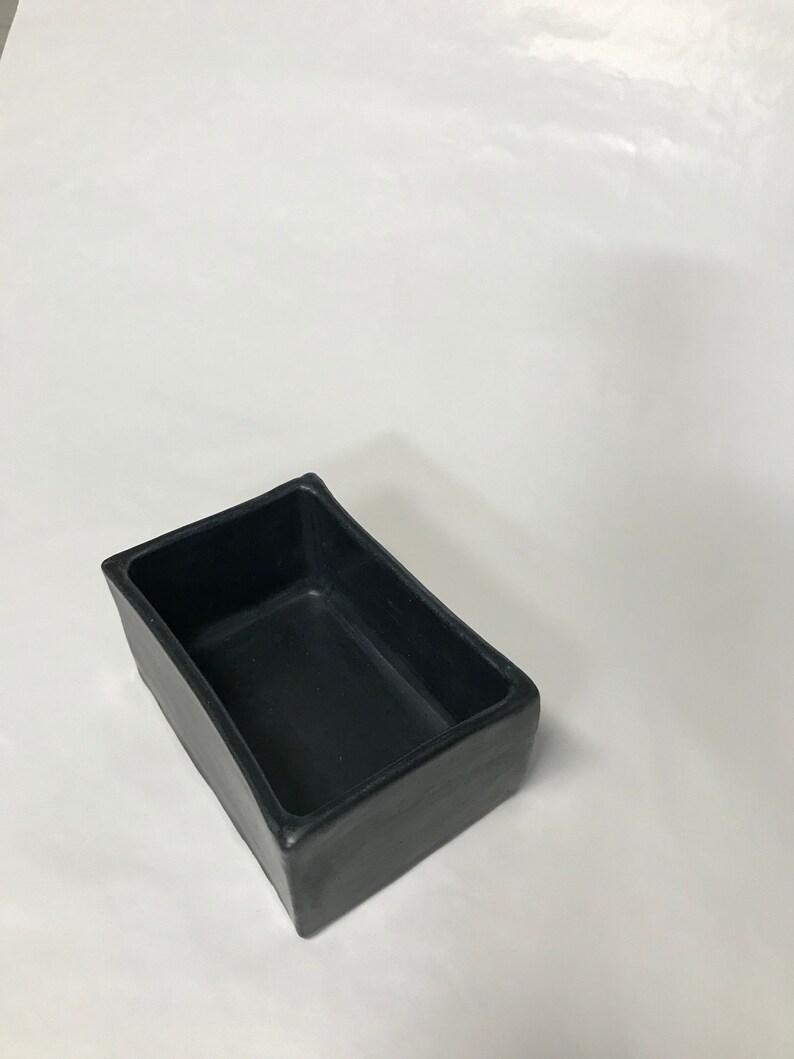 May include: A black rectangular ceramic planter with a smooth, slightly curved surface.