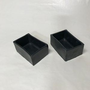 May include: Two black rectangular ceramic planters. The planters are made of a rough, textured material.