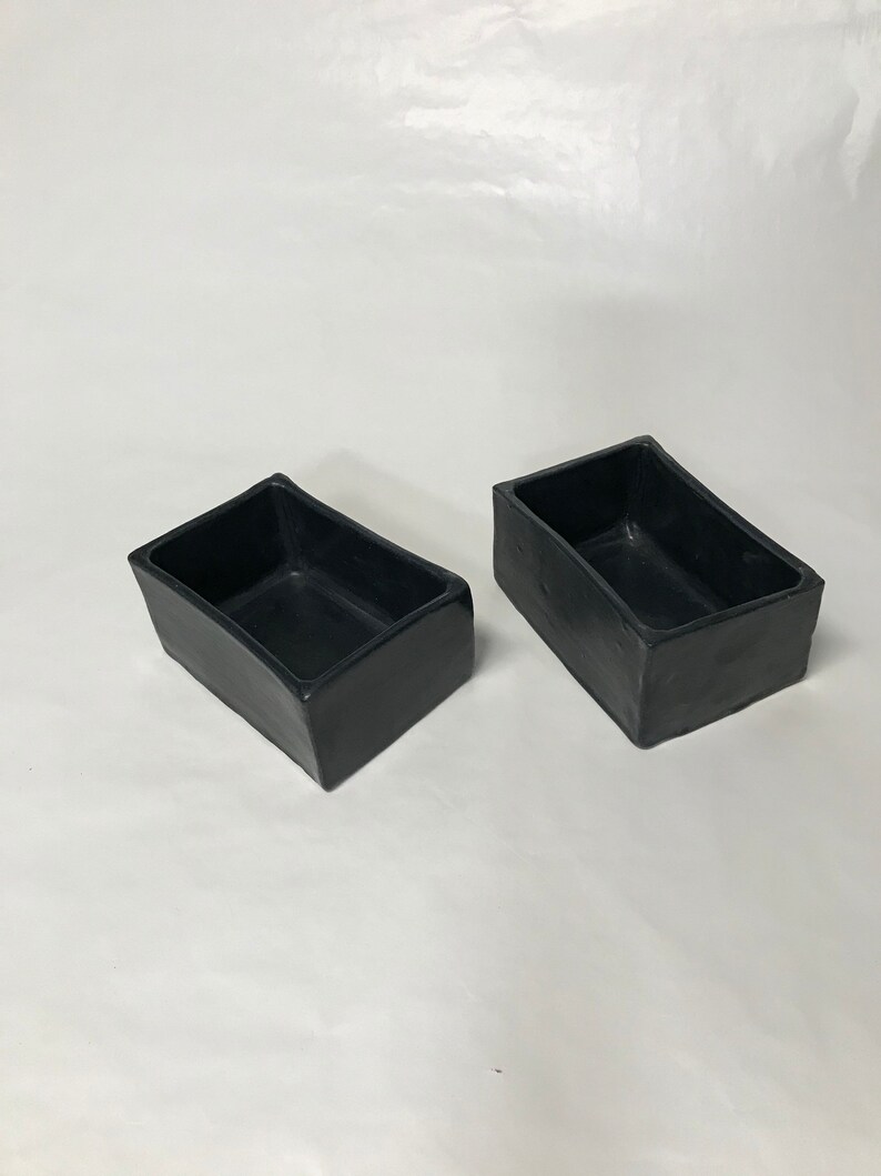 May include: Two black rectangular ceramic planters. The planters are made of a rough, textured material.
