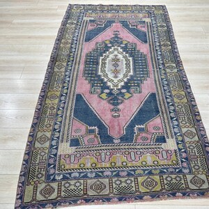 May include: A vintage rug with a pink, blue and yellow geometric pattern. The rug has a faded, distressed look and is perfect for adding a touch of bohemian style to your home.