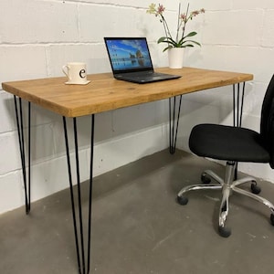 May include: A wooden desk with black hairpin legs and a black mesh office chair. A laptop computer and a white mug are on the desk.