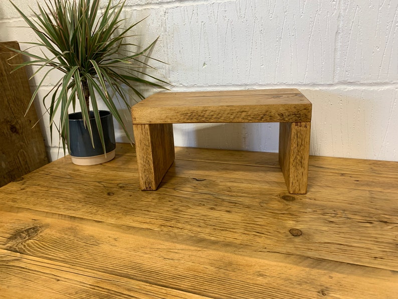 Puede incluir: Un taburete de madera r&uacute;stico con un acabado natural. El taburete est&aacute; hecho de madera reciclada y tiene un dise&ntilde;o simple y minimalista.