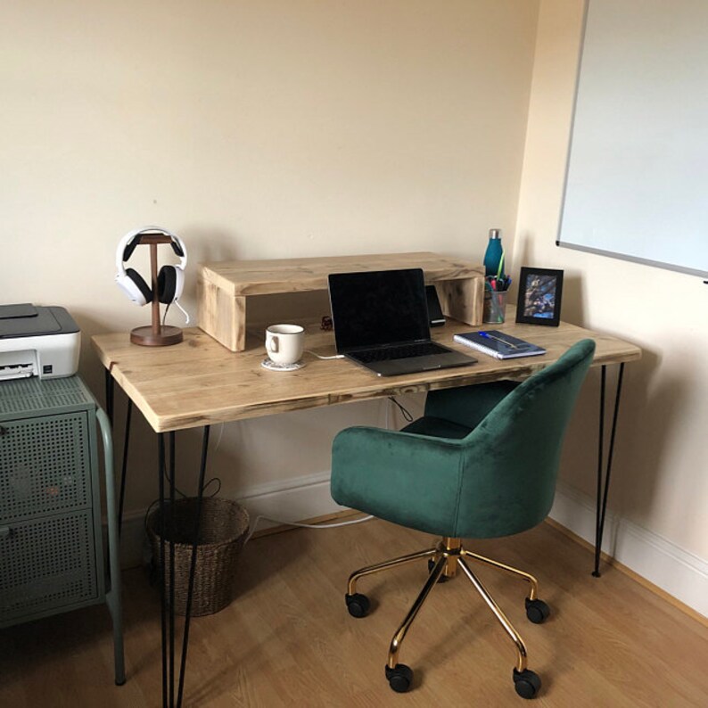 Puede incluir: Un escritorio de madera con patas de horquilla negras y una silla de oficina de terciopelo verde. El escritorio tiene un estante para una computadora port&aacute;til y una taza blanca est&aacute; sobre el escritorio.