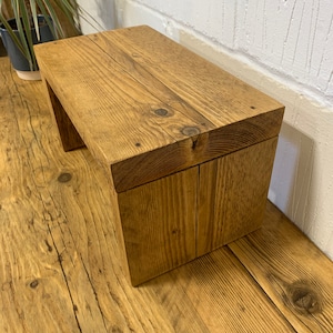Puede incluir: Un taburete de madera r&uacute;stico con un acabado de madera natural. El taburete est&aacute; hecho de madera reciclada y tiene un dise&ntilde;o simple y rectangular.