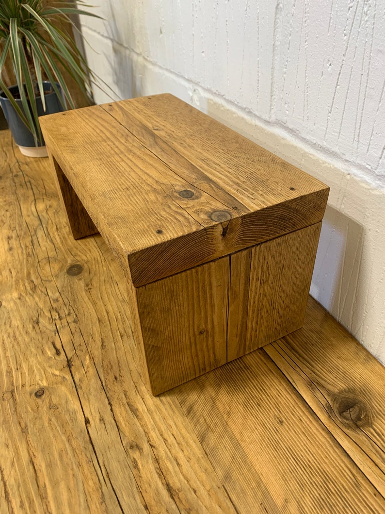 Puede incluir: Un taburete de madera r&uacute;stico con un acabado de madera natural. El taburete est&aacute; hecho de madera reciclada y tiene un dise&ntilde;o simple y rectangular.