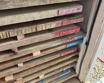 May include: A stack of weathered wooden planks, some with red and blue painted edges. The planks are arranged horizontally, showing signs of wear and tear, and are likely reclaimed or repurposed materials. The image suggests a rustic or industrial aesthetic.