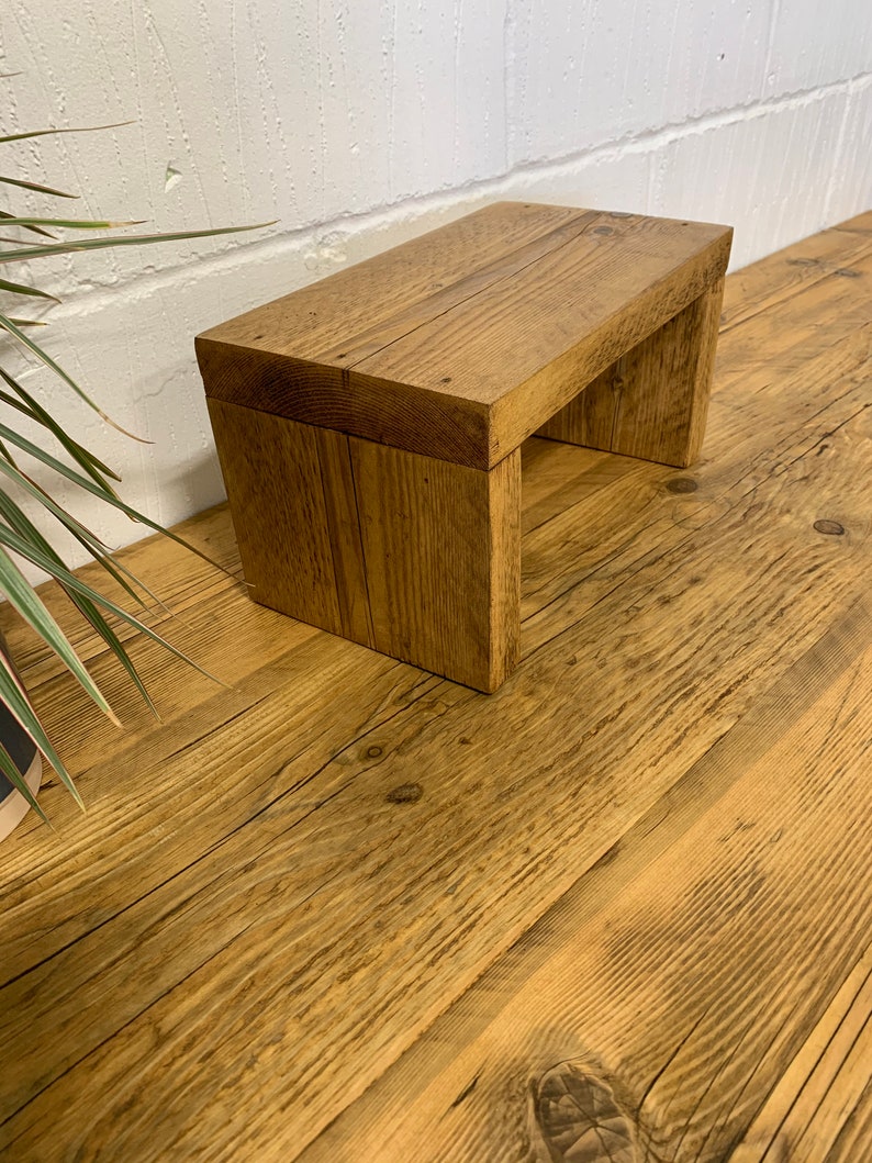 Puede incluir: Un peque&ntilde;o taburete de madera con un acabado de madera natural. El taburete est&aacute; hecho de madera reciclada y tiene un aspecto r&uacute;stico.