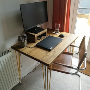 Puede incluir: Un escritorio de madera con un acabado marr&oacute;n claro y patas de horquilla amarillas. Un ordenador port&aacute;til, un monitor y un cactus est&aacute;n sobre el escritorio. Una silla de cuero marr&oacute;n con un marco de cromo est&aacute; al lado del escritorio.