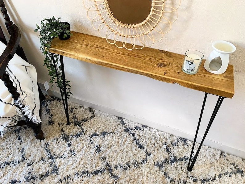 May include: A rustic wooden console table with hairpin legs. The table has a natural wood finish and is decorated with a candle and a diffuser. The table is sitting on a white shag rug.