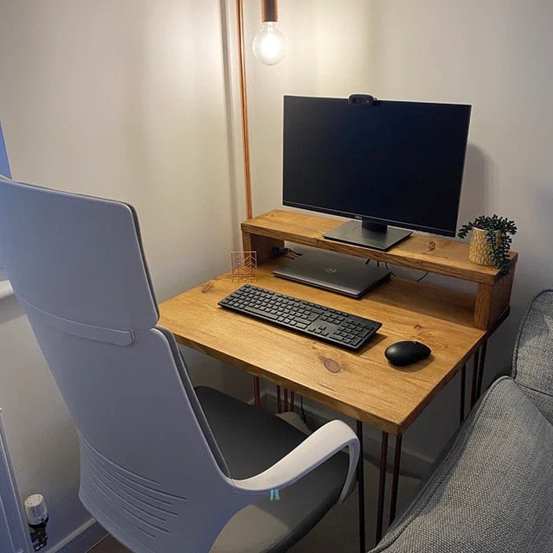 May include: A wooden desk with a light wood finish and black metal legs. The desk has a monitor stand and a keyboard on the surface. A white office chair is positioned in front of the desk.