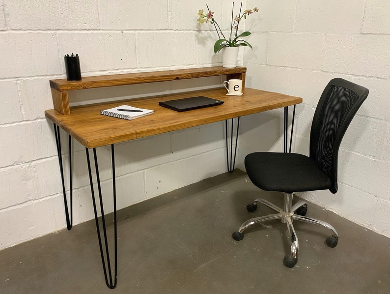 May include: A rustic wooden desk with a black metal shelf and hairpin legs. The desk has a notebook and pen on the surface, a laptop, and a small potted plant. A black mesh office chair with silver wheels is positioned next to the desk.