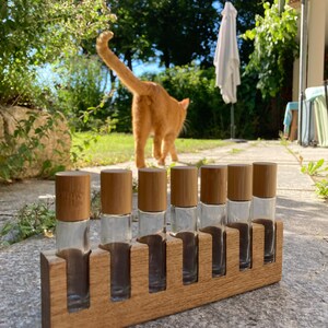 May include: A wooden rack with eight clear glass bottles with bamboo lids. The bottles are arranged in a row and are empty. The rack is sitting on a gray stone surface.