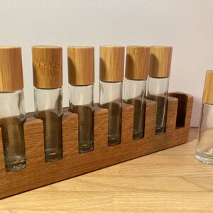 May include: A wooden stand with seven slots for holding small glass bottles with bamboo lids. The stand is made of light brown wood and the bottles are clear glass.