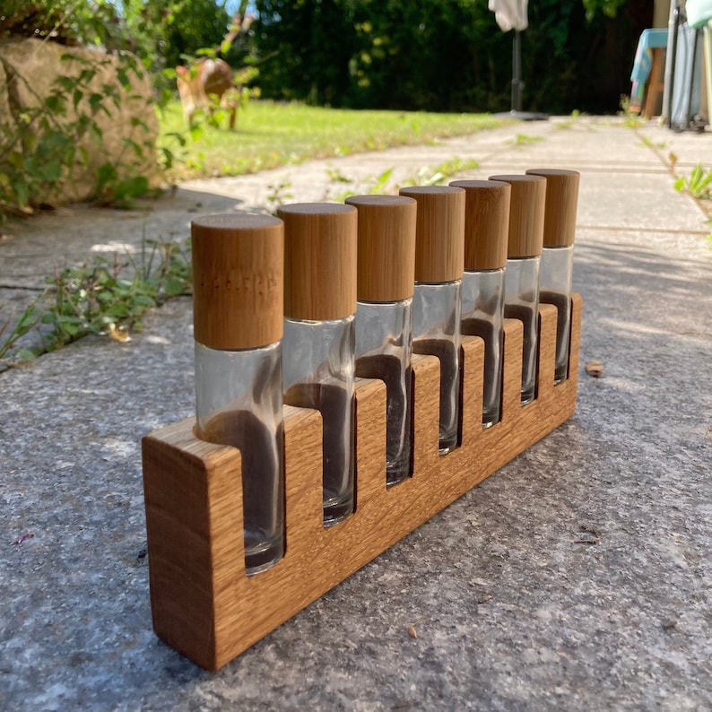 May include: A wooden rack with seven glass bottles with bamboo lids. The bottles are arranged in a row and are all the same size. The rack is made of light brown wood and has a natural finish.