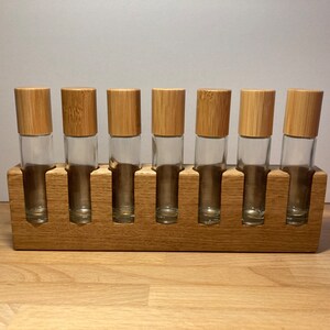 May include: A wooden stand with eight slots for holding essential oil roller bottles. The stand is made of light brown wood and has a natural finish. The bottles are clear glass with bamboo lids.