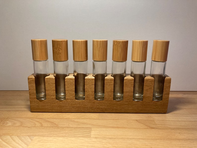 May include: A wooden stand with eight slots for holding essential oil roller bottles. The stand is made of light brown wood and has a natural finish. The bottles are clear glass with bamboo lids.
