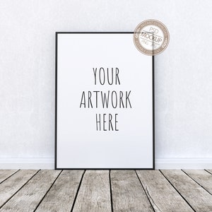 Peut inclure: Une maquette d'affiche encadrée en noir avec le texte "YOUR ARTWORK HERE" sur fond blanc. L'affiche est posée contre un mur blanc avec un sol en bois.