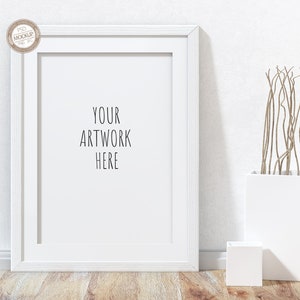 May include: White picture frame mockup with a white mat, on a white wall with a white vase and dried branches. The frame is empty and has the text "YOUR ARTWORK HERE" written on it.