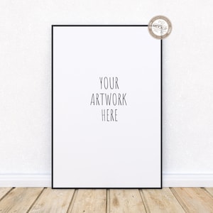May include: A black framed poster mockup with the text "YOUR ARTWORK HERE" on a white background. The poster is leaning against a white wall with a white baseboard and a wood floor.