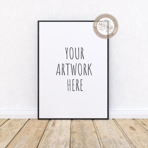 Peut inclure: Une maquette d'affiche encadrée en noir avec le texte "YOUR ARTWORK HERE" sur fond blanc. L'affiche est posée contre un mur blanc avec un sol en bois.