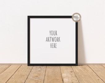 Könnte beinhalten: Ein quadratischer schwarzer Bilderrahmen mit dem Text "YOUR ARTWORK HERE" auf weißem Hintergrund. Der Rahmen lehnt an einer weißen Wand auf einem Holzboden. Ein kleiner runder Aufkleber befindet sich in der oberen rechten Ecke.