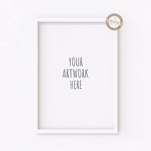 以下が含まれることがあります： 白い壁に「YOUR ARTWORK HERE」というテキストが書かれた白い写真フレームのモックアップです。