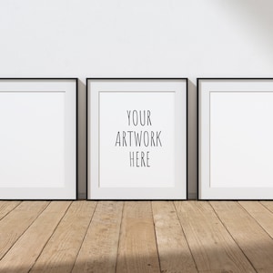 Peut inclure: Trois images encadrées noires avec des passe-partout blancs accrochées à un mur blanc au-dessus d'un sol en bois. L'image du milieu porte le texte "YOUR ARTWORK HERE" en noir.