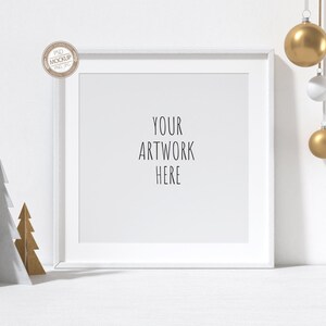 May include: White picture frame with a white mat and the text "YOUR ARTWORK HERE" on a white background. Two small paper Christmas trees are in the foreground, one white and one gold. Three ornaments hang from the top of the frame, one gold, one white, and one gold.