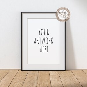 May include: A black picture frame with a white mat, hanging on a white wall. The frame is empty, with the text "YOUR ARTWORK HERE" written in black on the white mat.