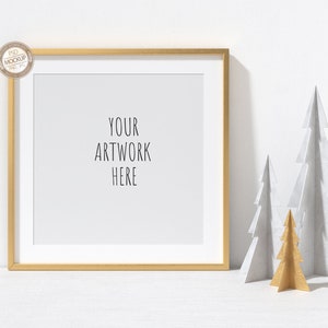 May include: A gold picture frame with a white mat and the text "YOUR ARTWORK HERE" on a white background. Three paper Christmas trees are in the foreground, two are white and one is gold.